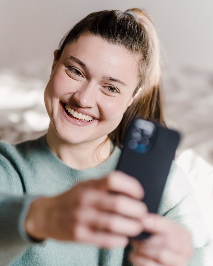 A casual selfie: a smiling woman in a green sweater, holding a phone.